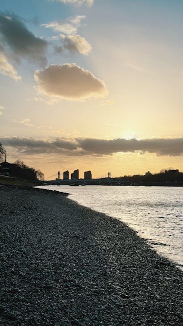 A stone archway forming a pedestrian and vehicle access point on Hammersmith Bridge, featuring a steel suspension design with green-painted railings and support cables. The bridge’s deck is visible 