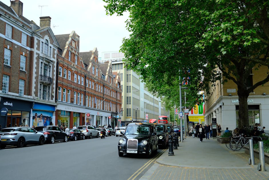 A quiet residential street in Hammersmith, featuring a row of Victorian-style terraced houses with white facades, bay windows, and red-tiled roofs. The pavement runs alongside the road, which has clea